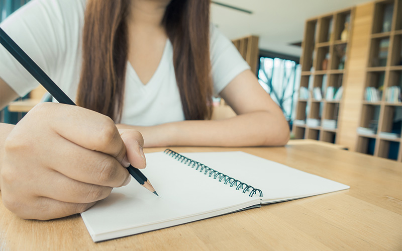 Student writing in a notebook with a pencil.
